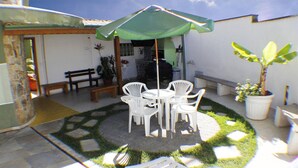 Eine Terrassengruppe im Freien mit rundem Tisch, Stühlen, einem grünen Sonnenschirm und Topfpflanzen.