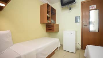 A small, single-bed room with a wooden wardrobe, a small refrigerator, and a television mounted on the wall.