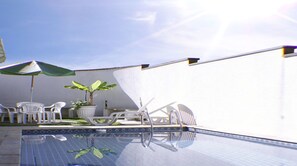 Una piscina al aire libre, sombrillas, sillones reclinables de piscina
