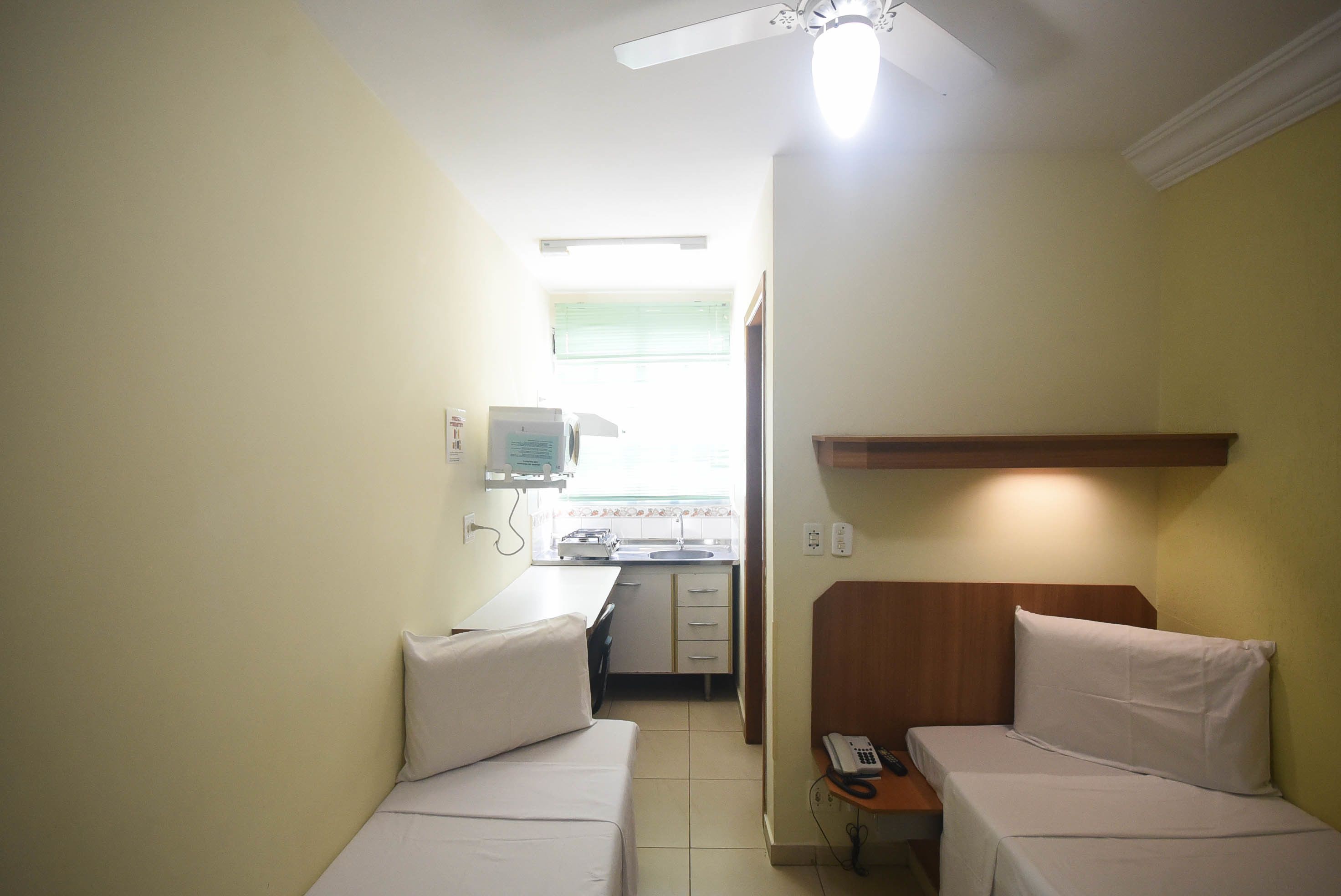 A small, single-room accommodation with two beds, a kitchenette, and a ceiling fan.