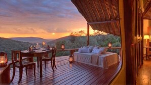 Una terrazza in legno con un letto, un tavolo da pranzo e sedie, con vista su un paesaggio montano.
