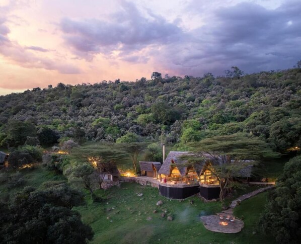 A secluded eco-lodge with thatched-roof cabins surrounded by lush greenery, set against a backdrop of a forested hillside.