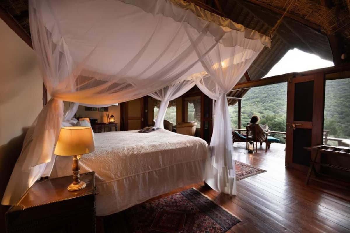 A bedroom with a canopy bed, a bedside lamp, a wooden nightstand, and a view of the outdoors.