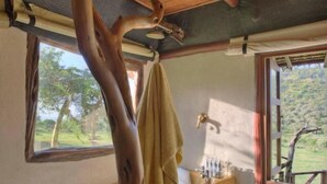 Interno rustico di una baita con soffitto in legno, una vasca da bagno piena di bolle, una finestra con vista su del verde e un asciugamano appeso a una trave di legno.