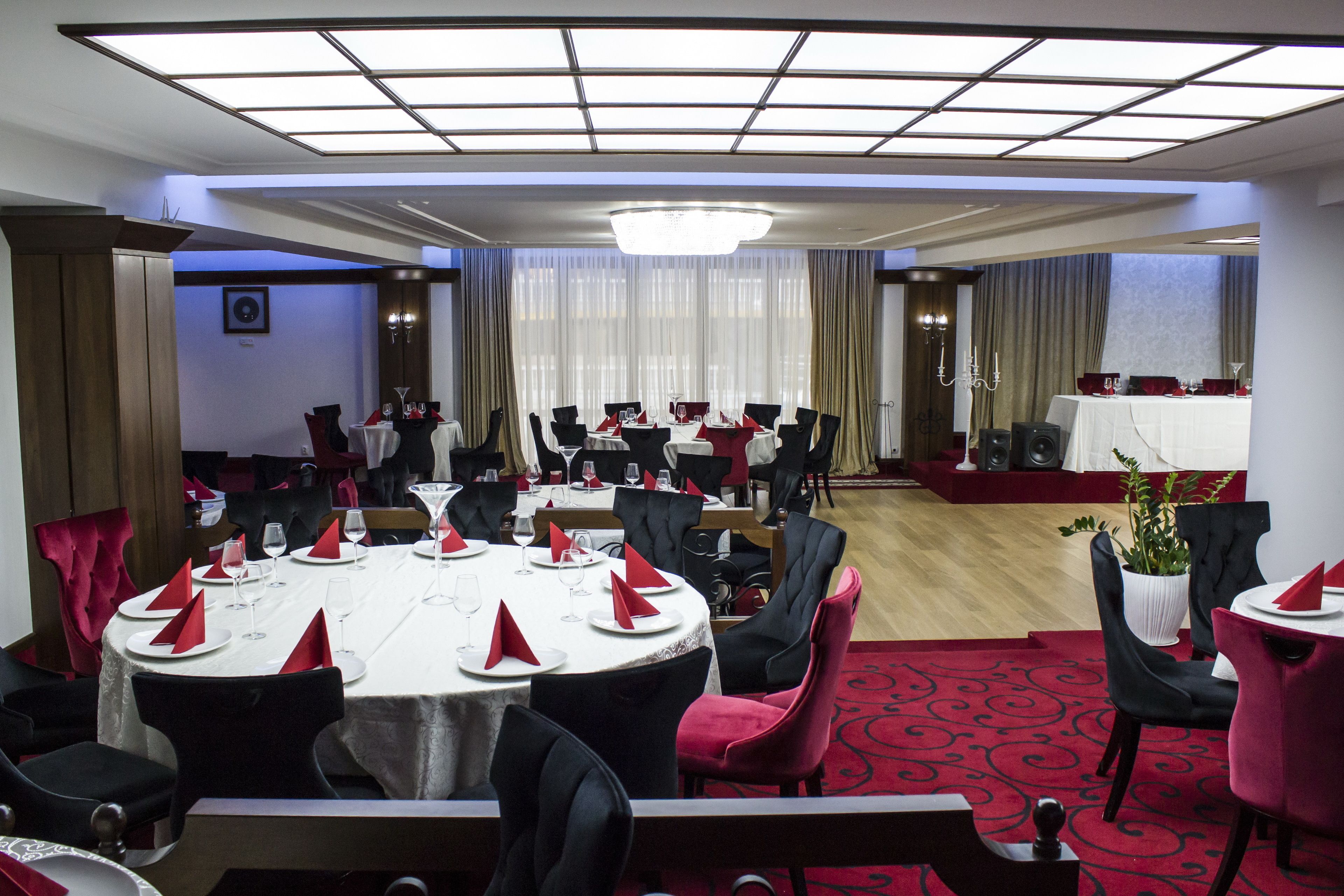 A hotel dining area with round tables, black and red chairs, and a red carpet.