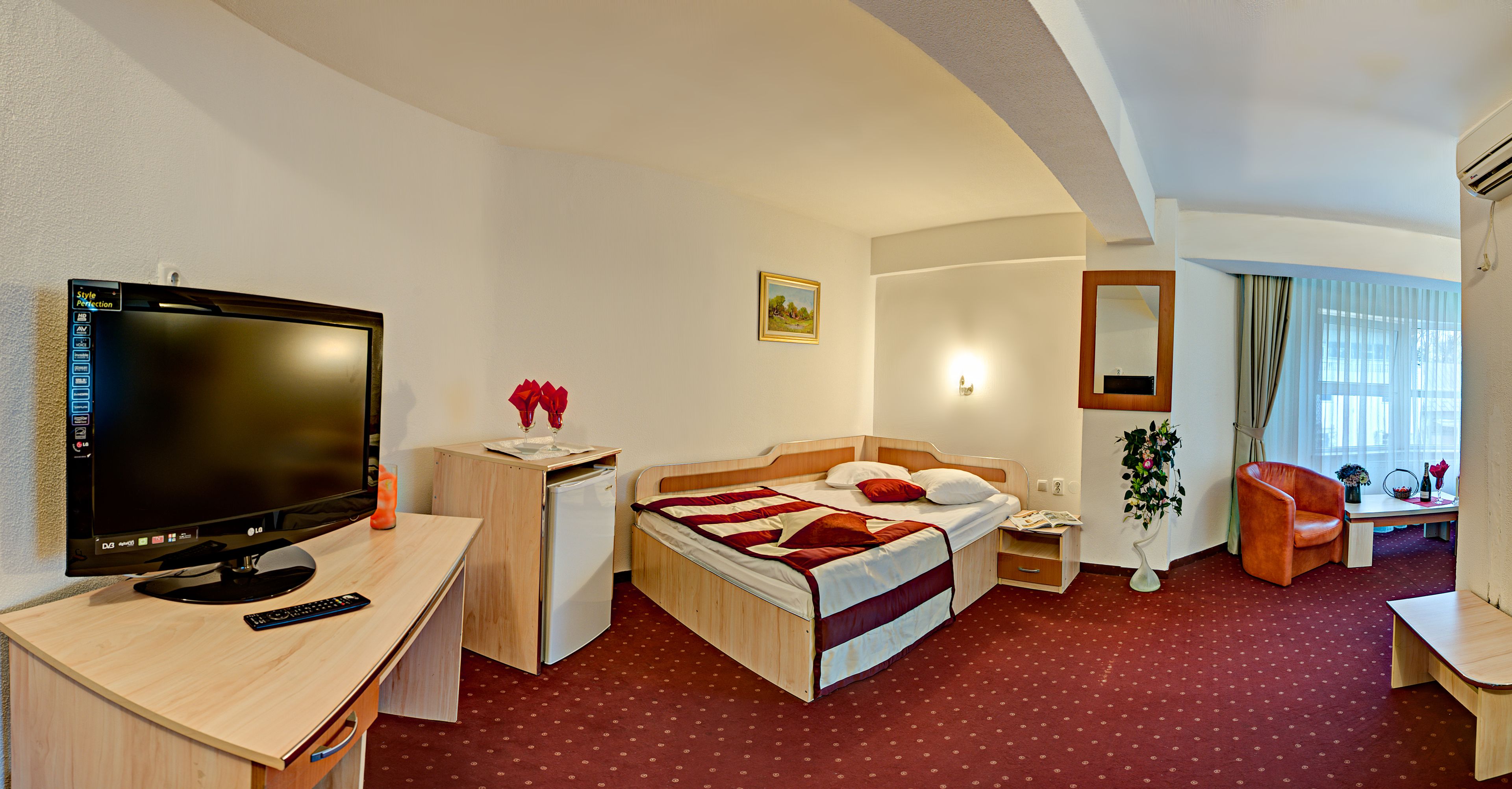 Habitación de hotel con cama, escritorio, televisor y un refrigerador pequeño.