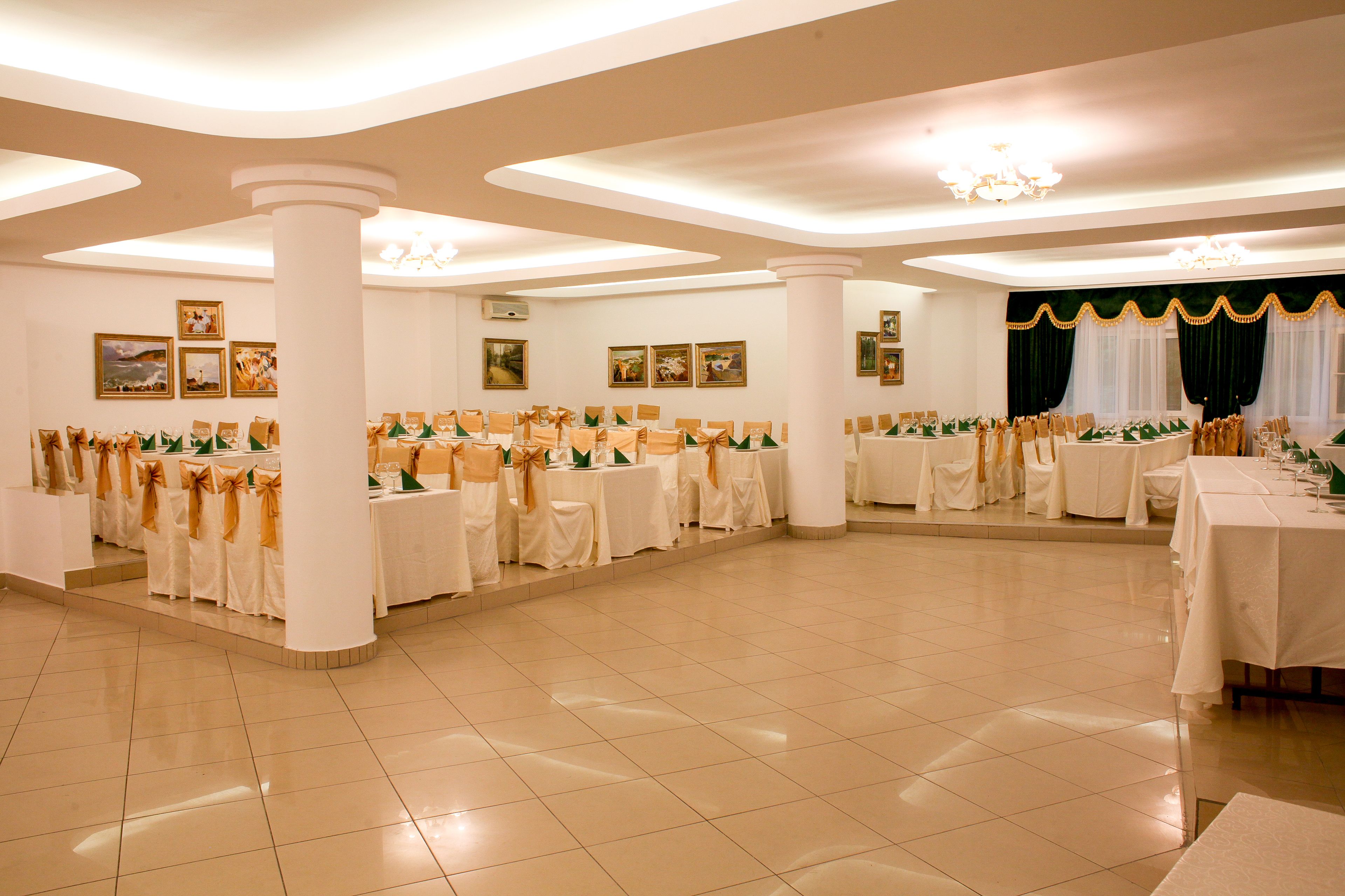 Un amplio salón de banquetes con varias mesas redondas, manteles blancos y sillas con cintas doradas.