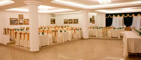 Un amplio salón de banquetes con varias mesas redondas, manteles blancos y sillas con cintas doradas.