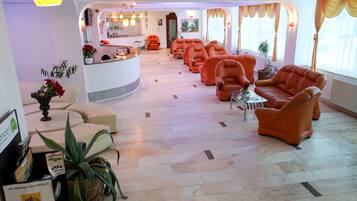 Un vestíbulo de hotel con un mostrador de recepción, varios sillones naranja, una mesa de centro y una planta grande en maceta.