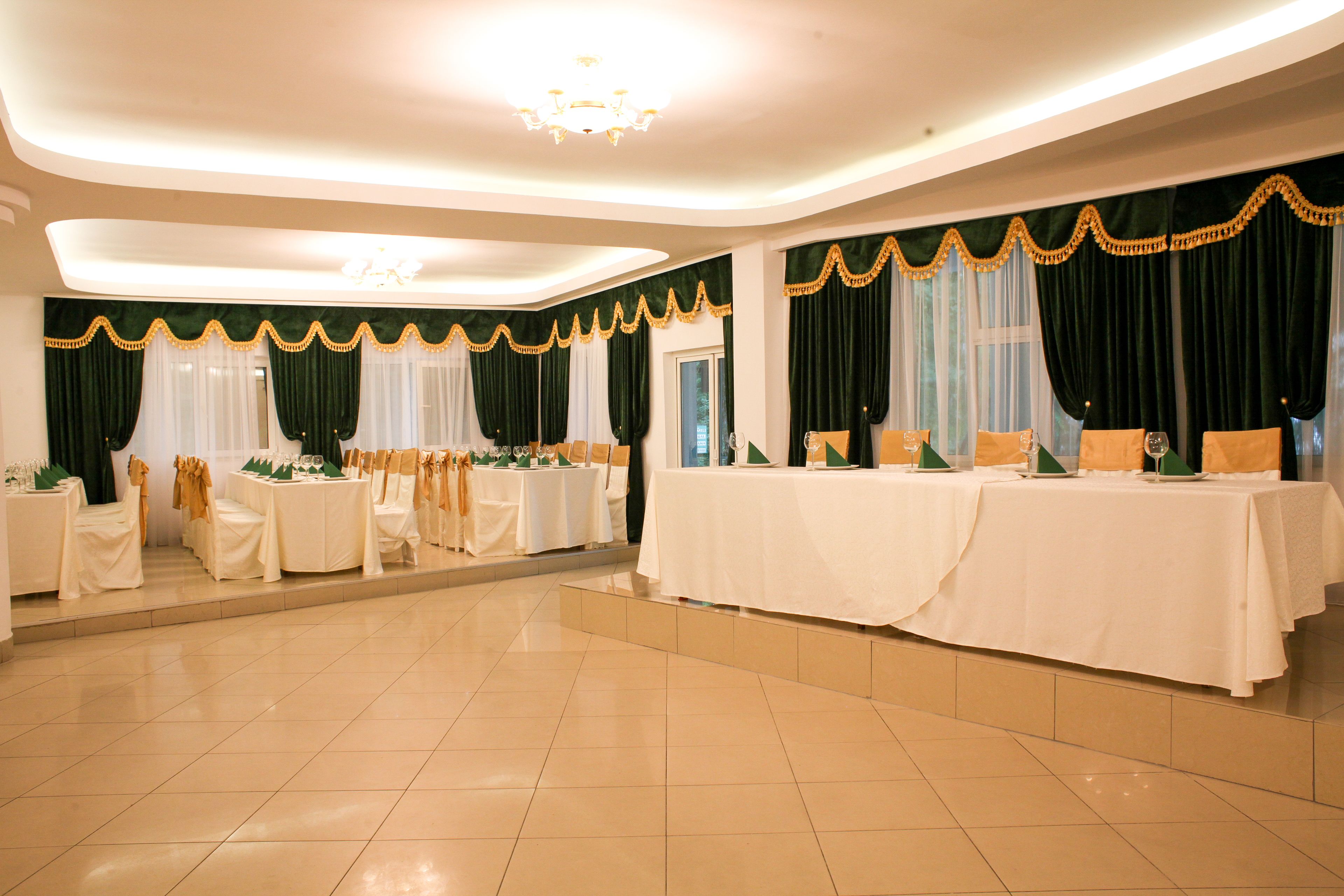 A spacious banquet hall with multiple round tables set for dining, adorned with white tablecloths and gold accents.