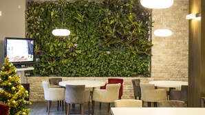 A modern indoor space with a green leafy wall, round tables, and chairs. - Complex Turistic Cornul Vanatorului (Pitesti)