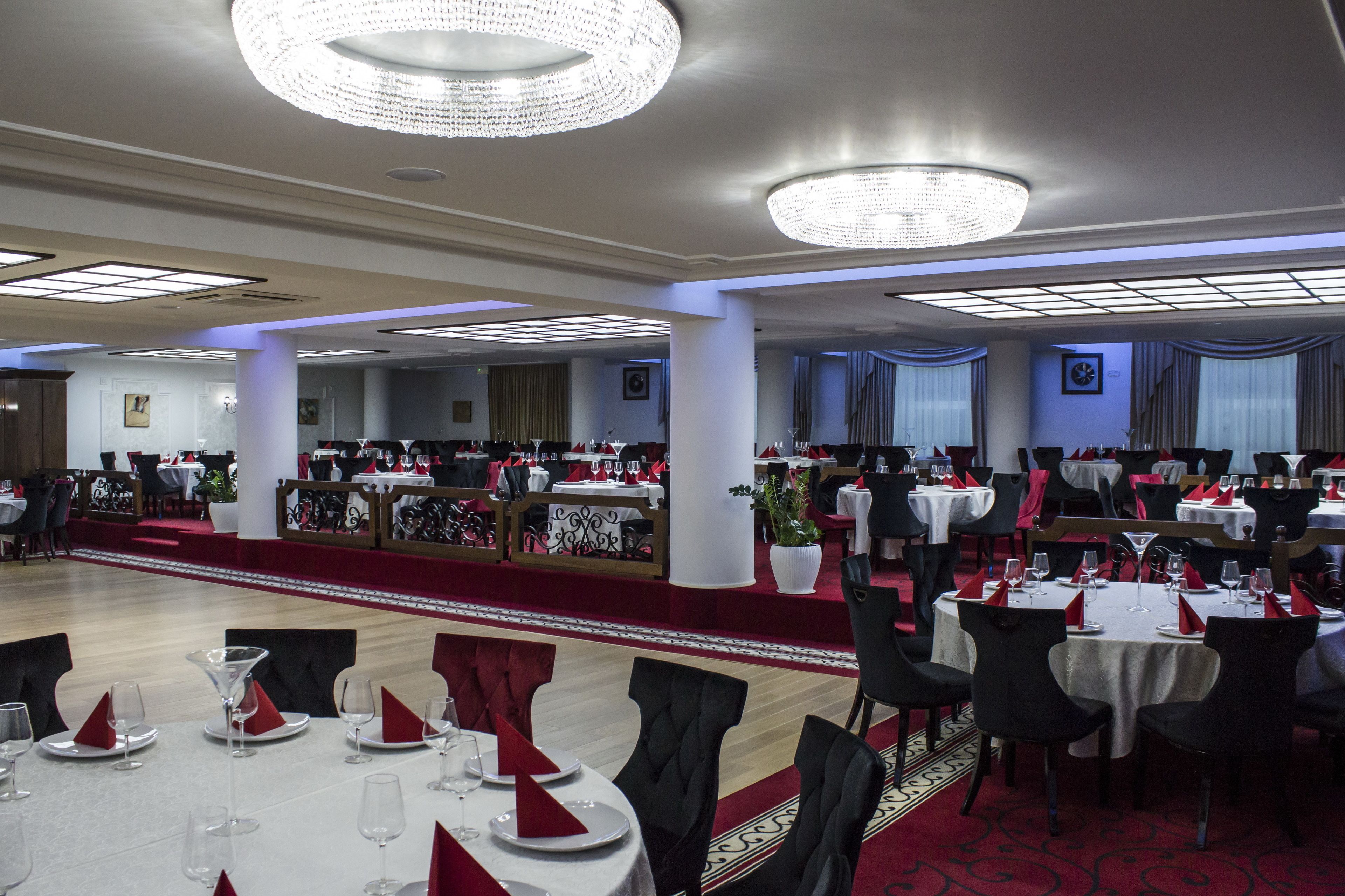 A banquet hall with round tables, red napkins, and chandeliers.