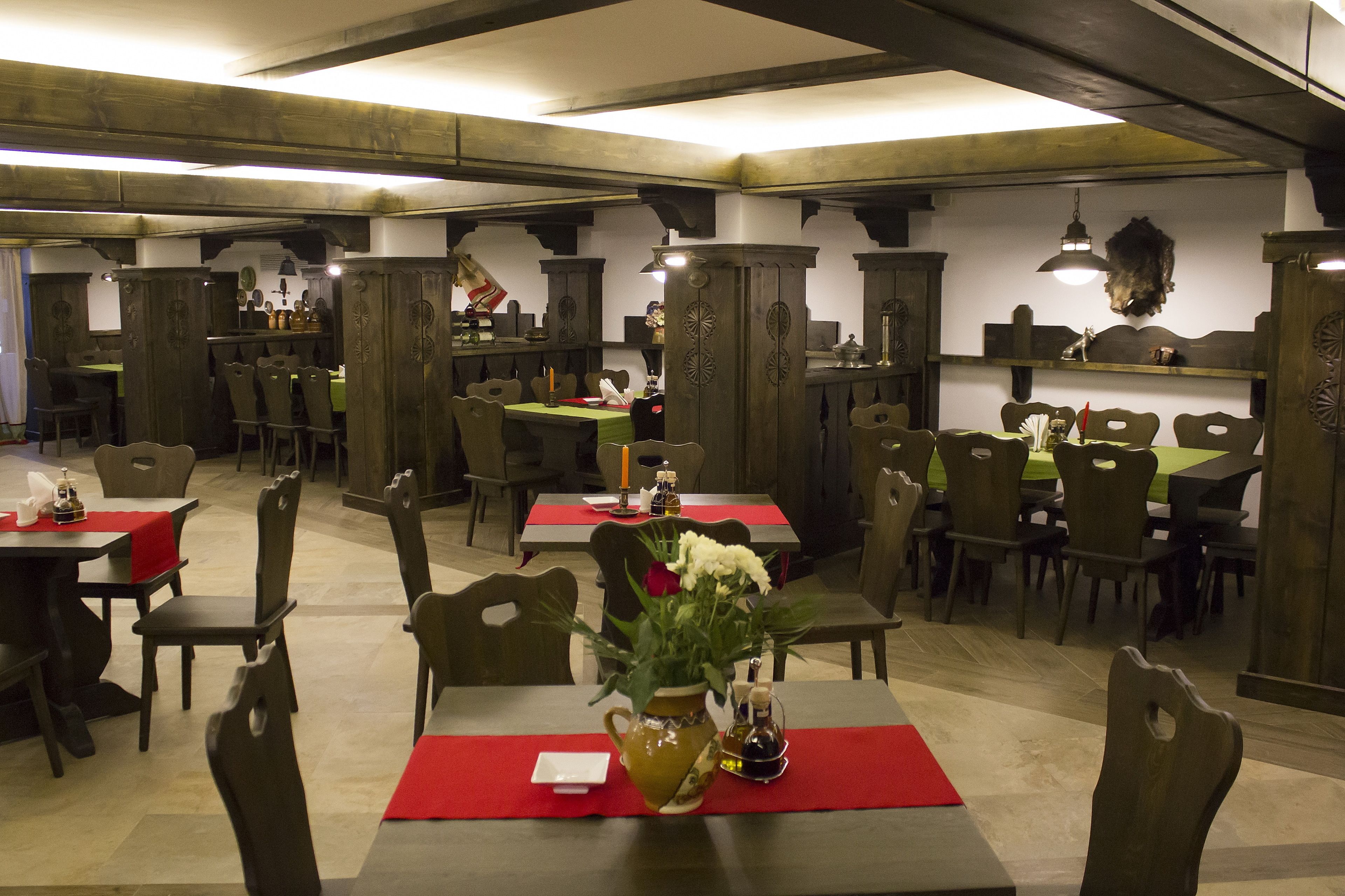 A restaurant with wooden furniture, red tablecloths, and a vase with flowers on the tables.