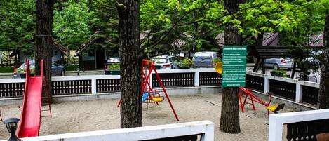 Un parque con juegos infantiles, bancos y árboles.