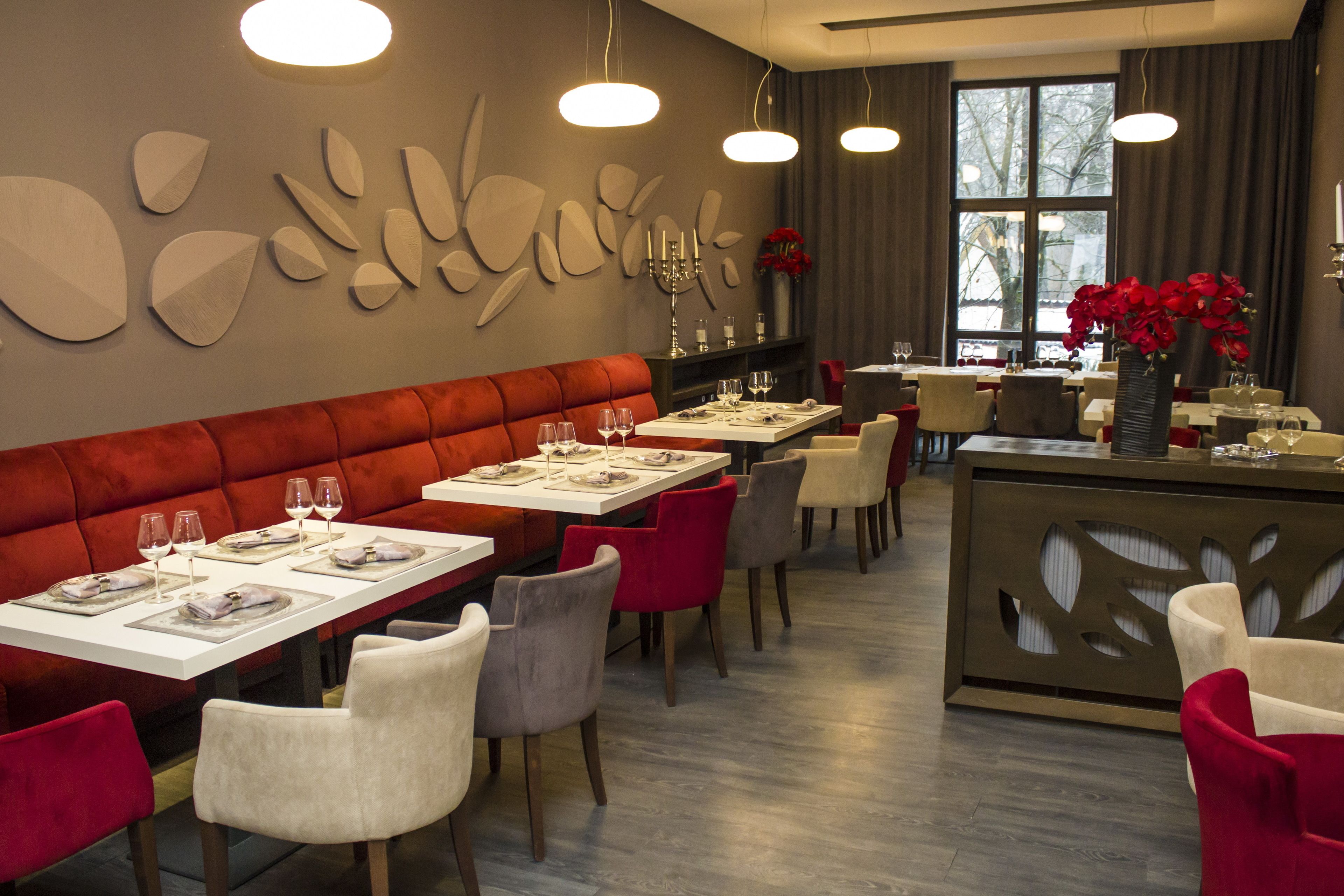 Ein Restaurant mit einer roten gepolsterten Bank, weißen Tischen und grauen Stühlen.