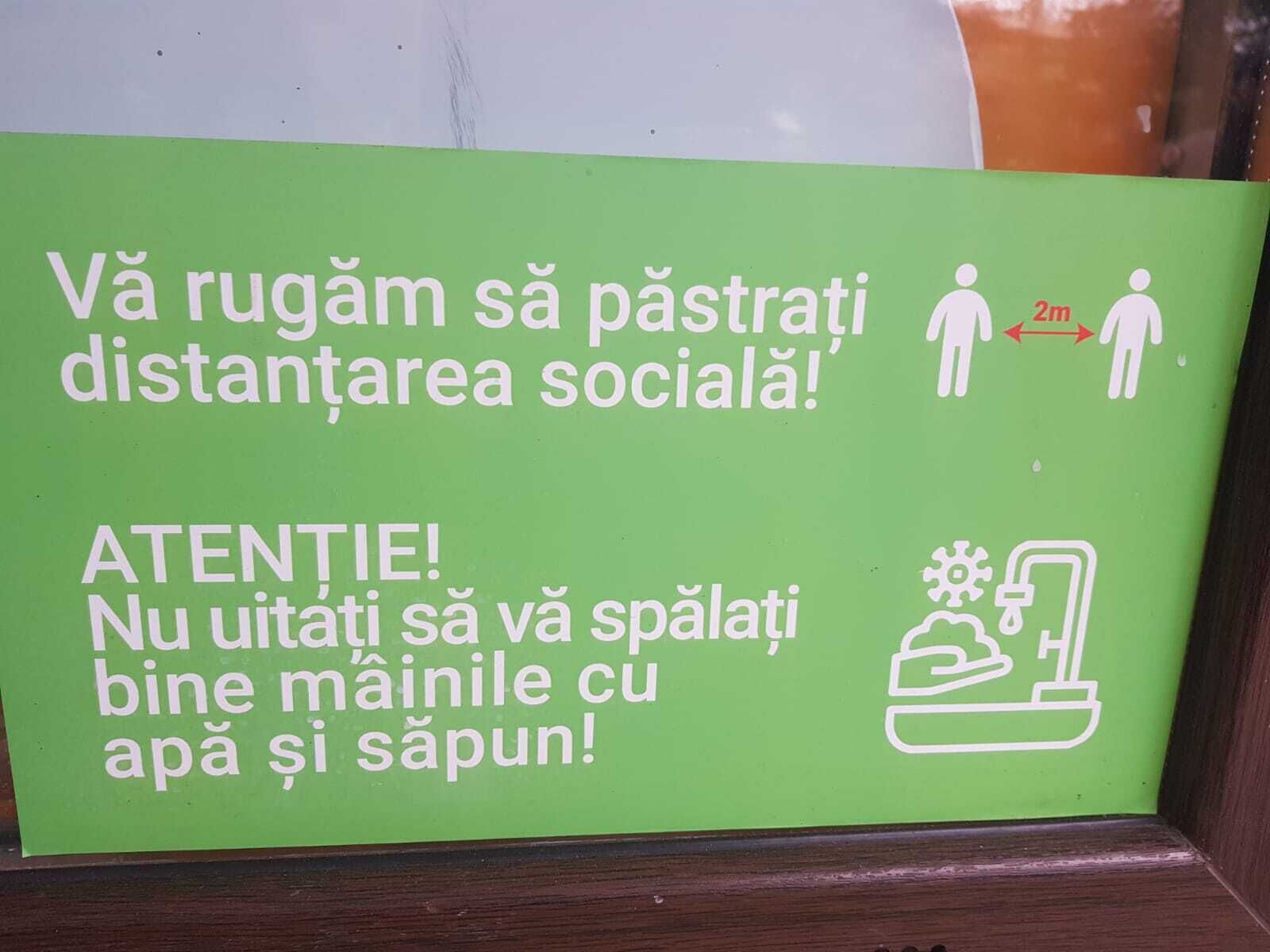 A green sign with white text and symbols, advising social distancing and hand washing.