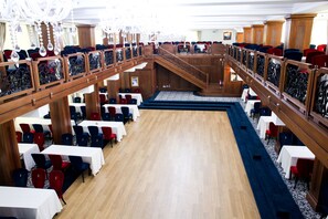 A spacious hall with multiple tables and chairs, a central staircase, and a chandelier. - Complex Turistic Cornul Vanatorului (Pitesti)