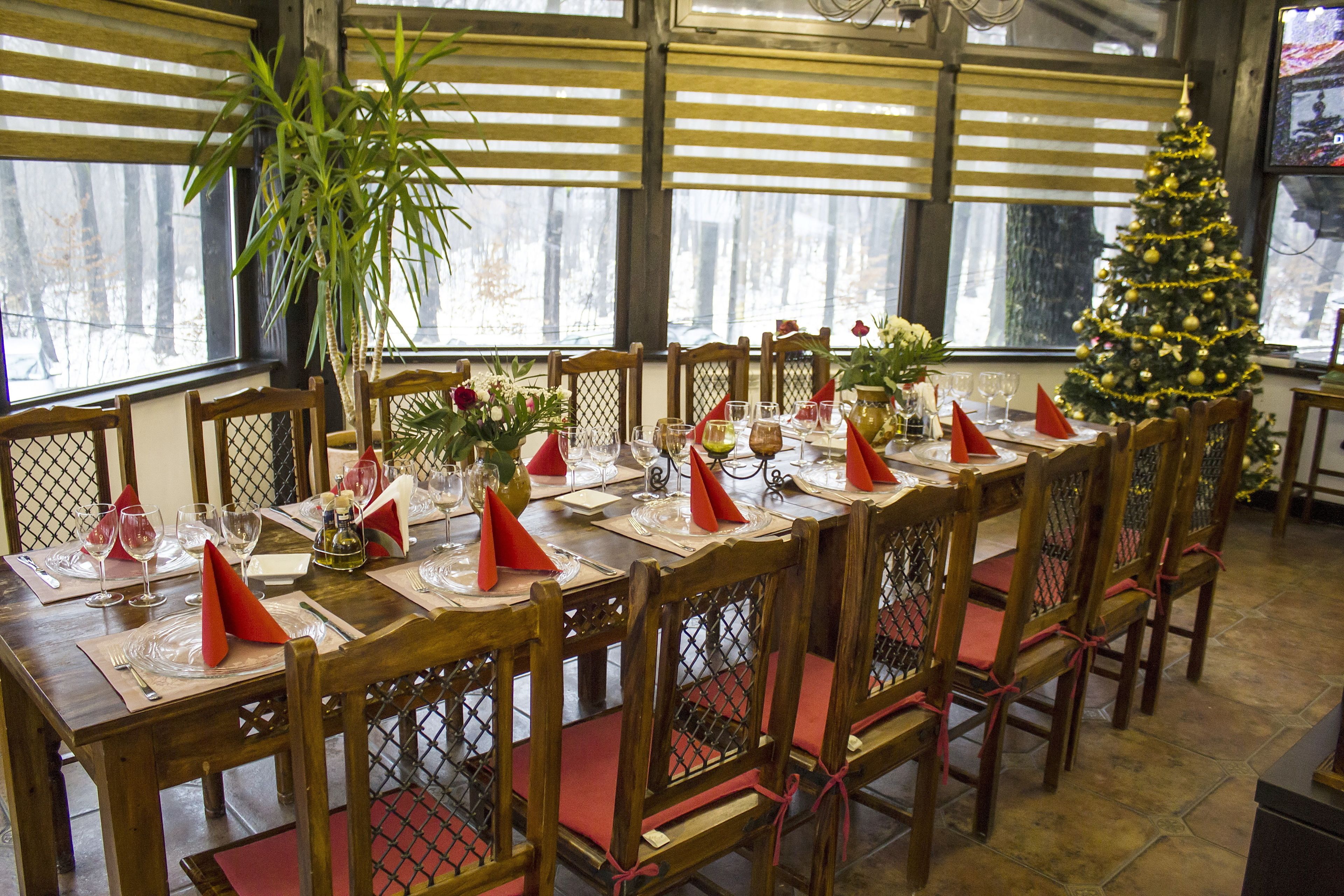 A dining area with a long wooden table set for a meal, surrounded by chairs with red cushions.