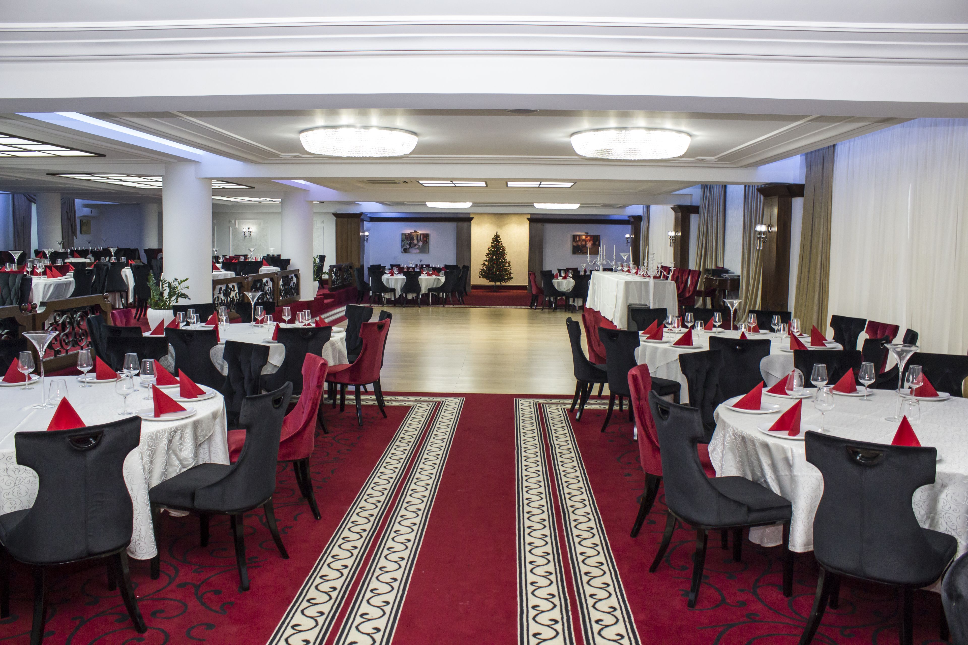 A large banquet hall with round tables, red and white tablecloths, and black chairs.