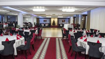 Un gran salón de banquetes con mesas redondas, manteles blancos y rojos y sillas negras.