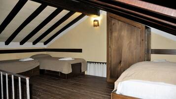Ein Zimmer mit schrägverlaufender Decke, Holzbalken, einem Bett, zwei kleineren Betten und einer Wandleuchte.