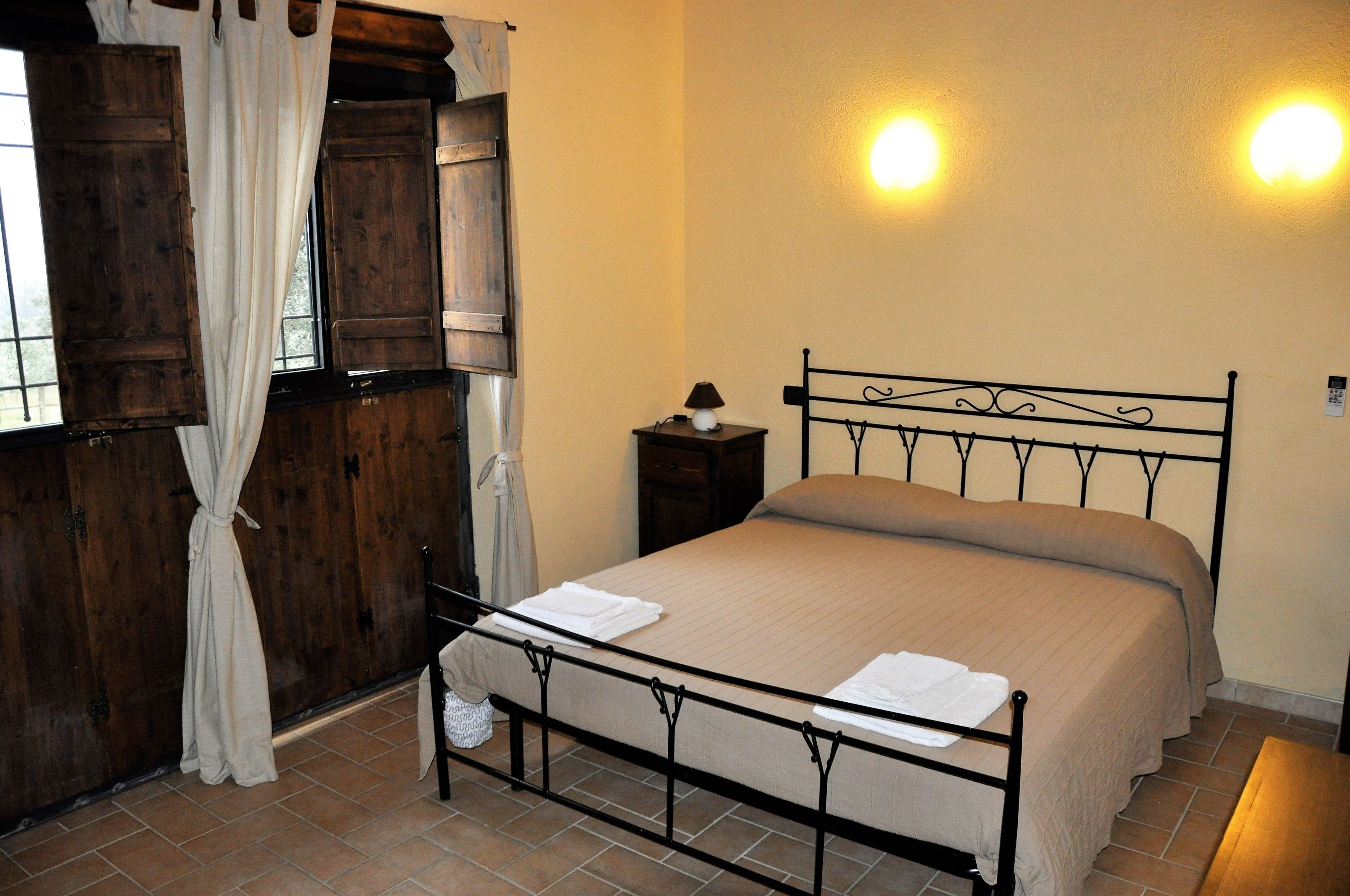A bedroom with a metal bed frame, a wooden wardrobe, and a nightstand with a lamp.