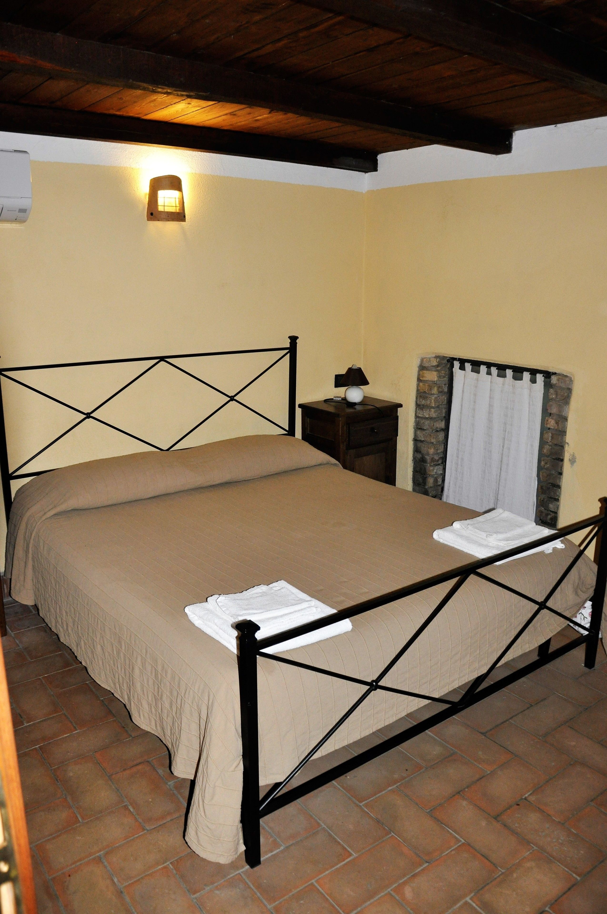 A single bed with a metal frame, a bedside table with a lamp, and a curtain on the window.