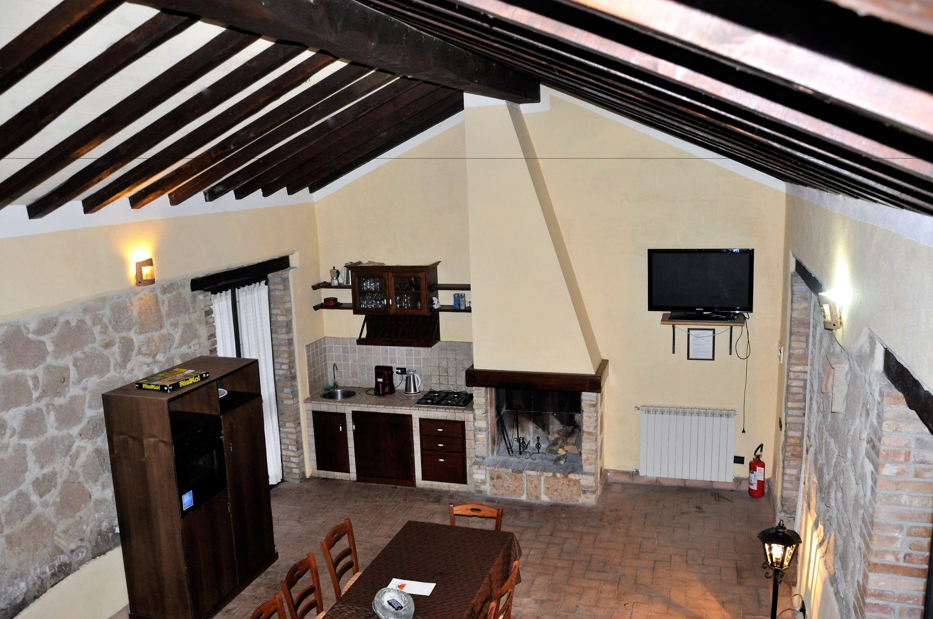 A cozy outdoor kitchen area with a stone fireplace, a television mounted on the wall, and a wooden table with chairs.