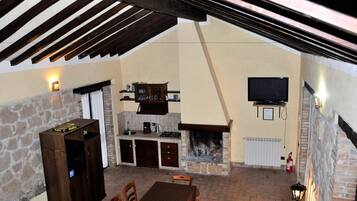 A cozy outdoor kitchen area with a stone fireplace, a television mounted on the wall, and a wooden table with chairs.