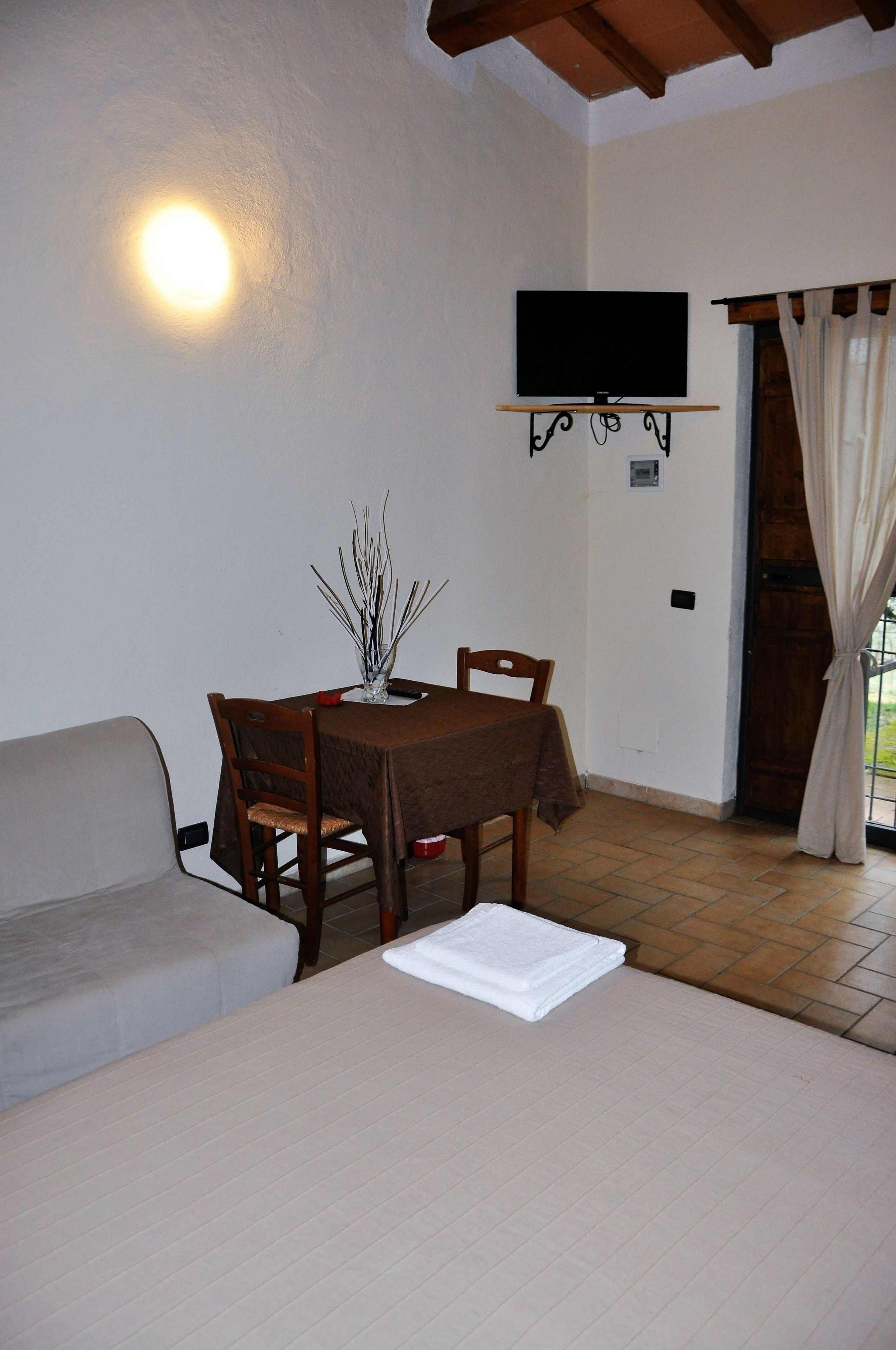 A cozy room with a bed, a sofa, a dining table with chairs, a flat-screen TV mounted on the wall, and a door with curtains.