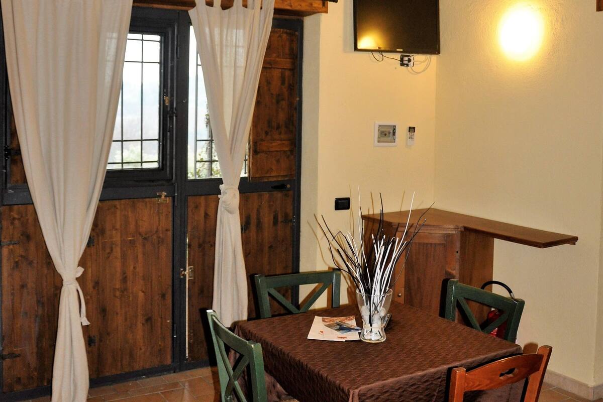 A dining area with a table set for two, wooden chairs, a wall-mounted TV, and an air conditioning unit.