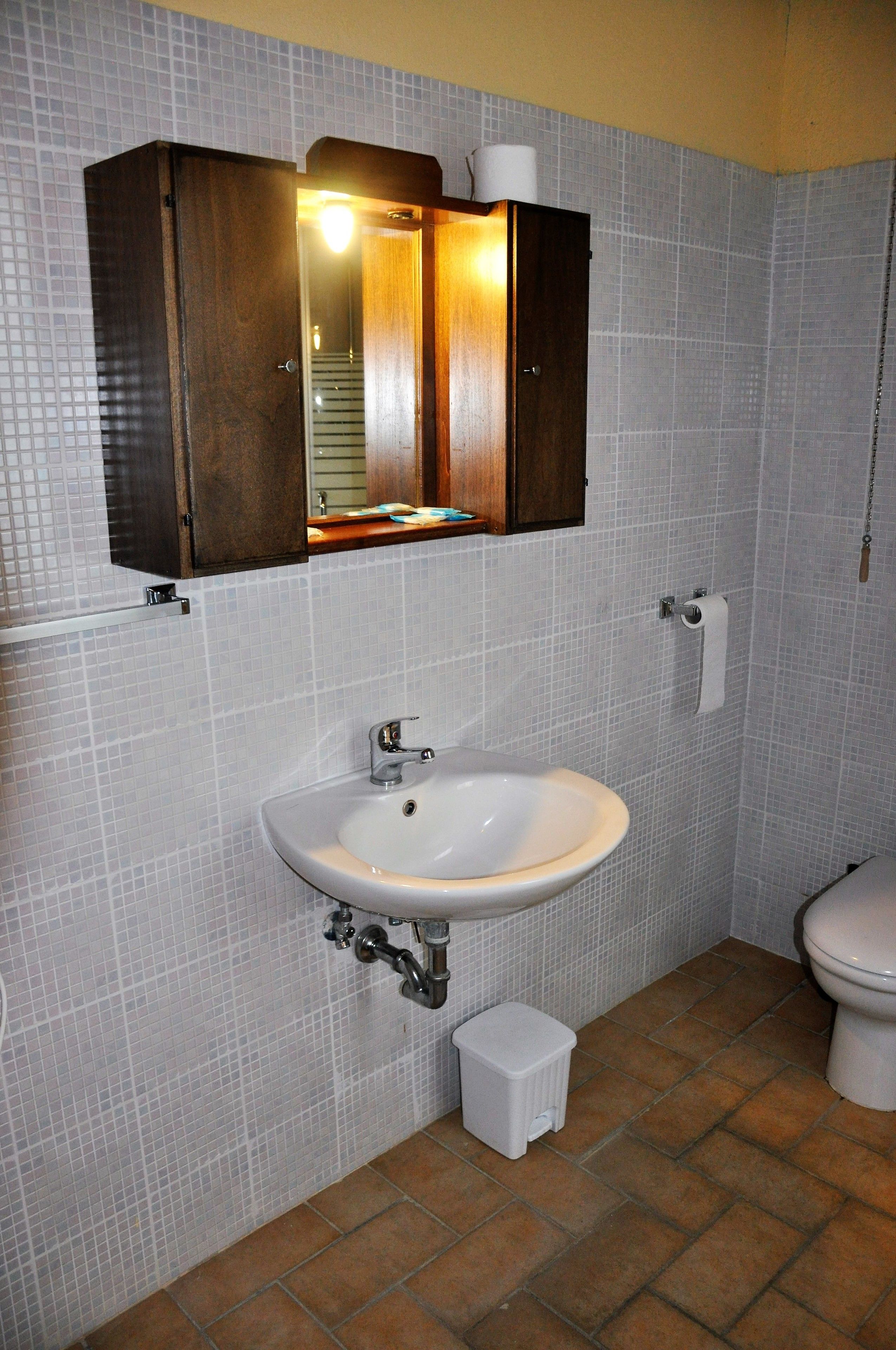 A bathroom with a white sink, a wooden cabinet above it, and a toilet.