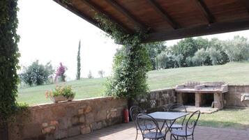 Un patio al aire libre con paredes de piedra, una zona cubierta con techo de madera y una parrilla.