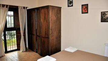 A room with a wooden wardrobe, a bed with a white sheet, and a window with curtains.