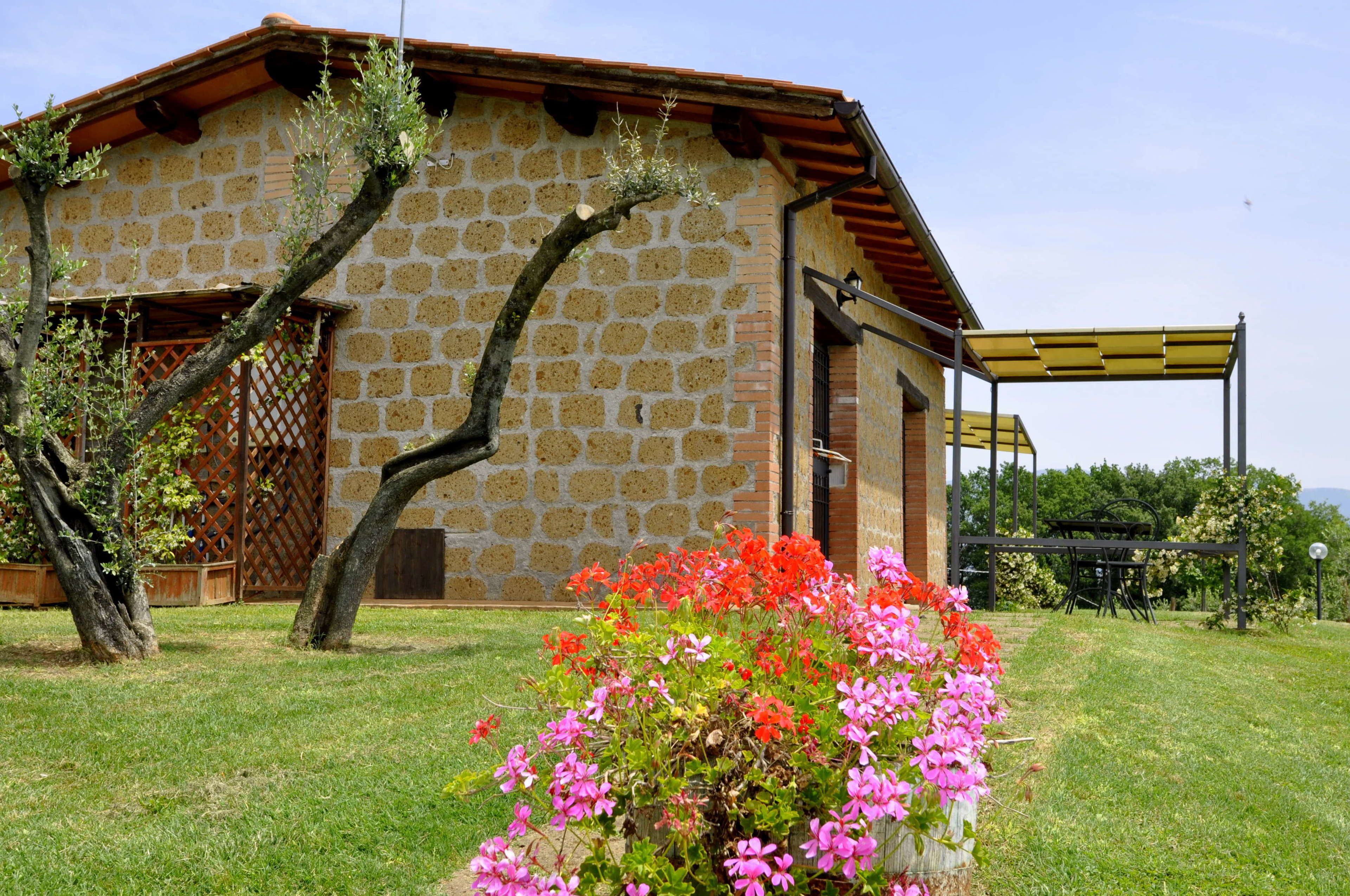 A stone building with a sloped roof, a wooden door, and a garden with flowering plants.