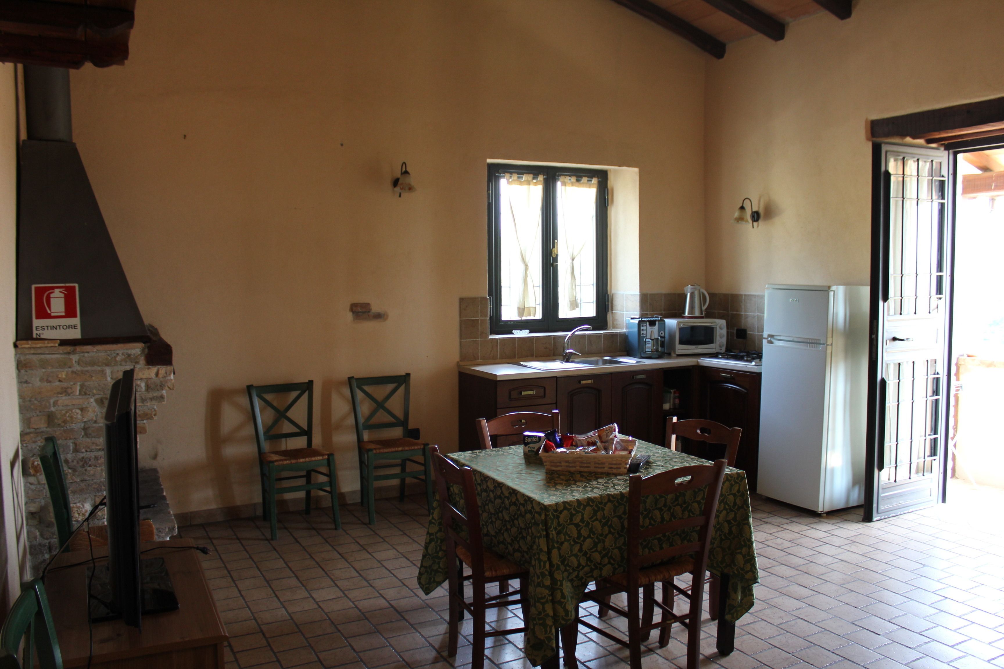 Une cuisine équipée d’une table à manger, de chaises, d’un réfrigérateur, d’un four à micro-ondes et d’une fenêtre avec des rideaux.