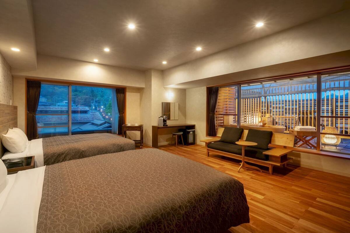 Une chambre d’hôtel avec deux lits, un bureau, un canapé et de grandes fenêtres donnant sur des immeubles.