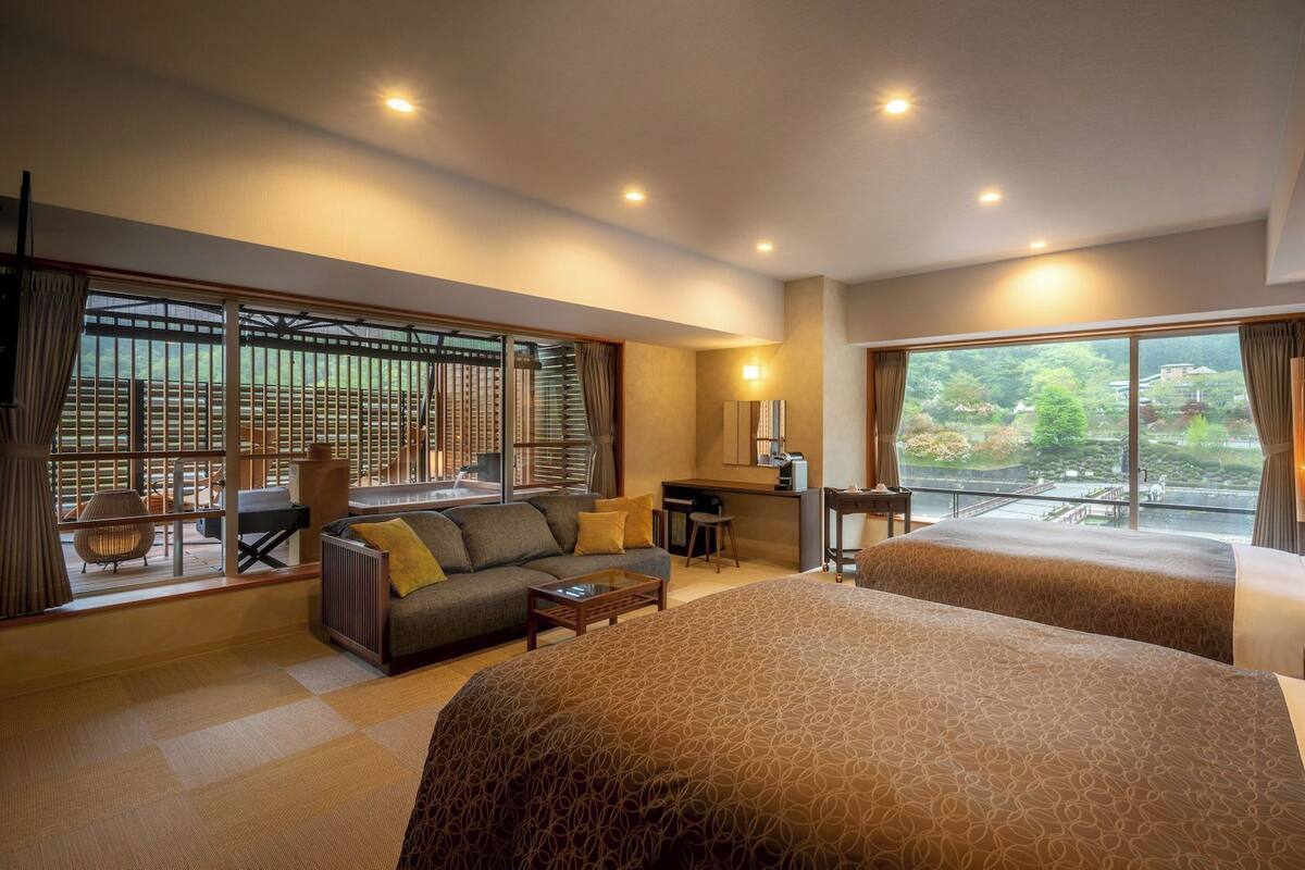 Une chambre d’hôtel avec un grand lit, un canapé, un bureau et une vue sur la verdure.