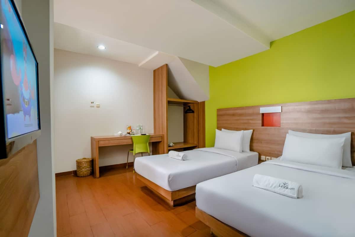 A hotel room with two beds, a desk, a chair, and a television.