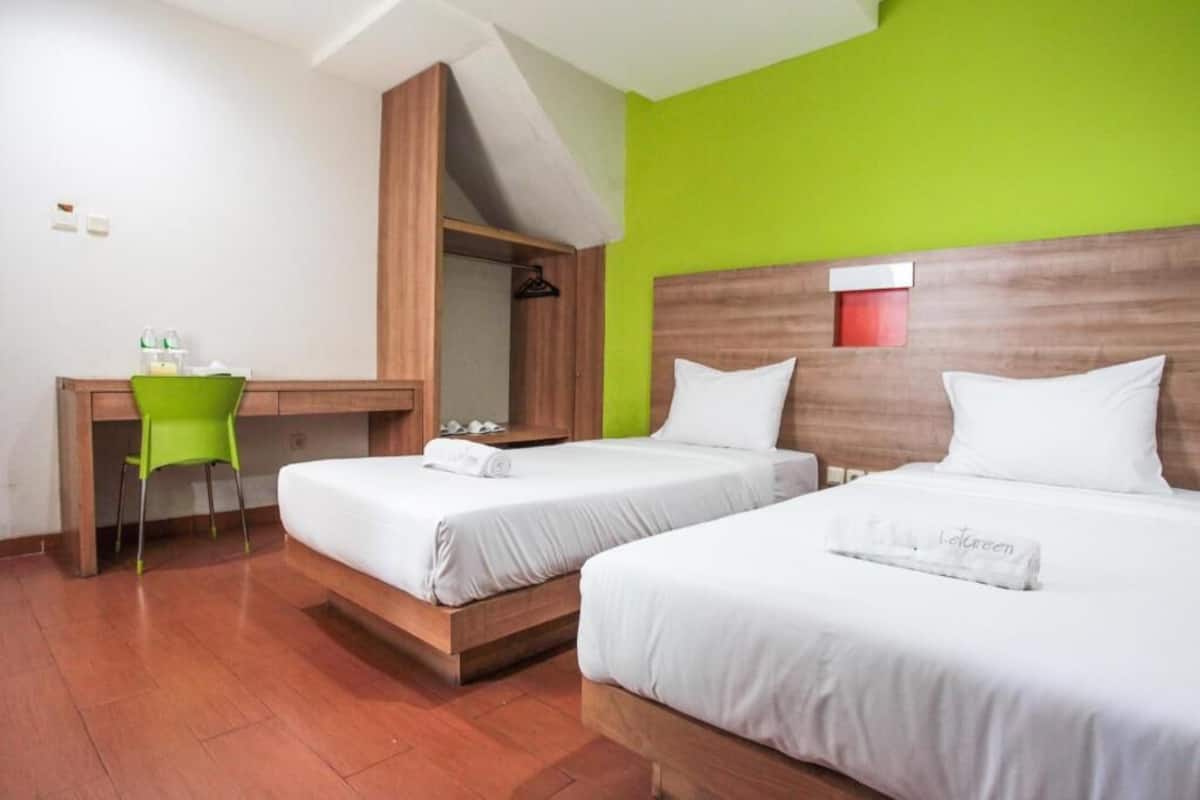 A hotel room with two beds, a desk, and a green chair.