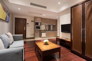 A compact living space with a sofa, a coffee table, a TV, a kitchenette, and a wardrobe.