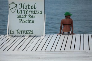 Hotelli La Terrazza -ravintolan ja uima-allasbaarin kyltti puukannella veden äärellä.