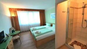 Habitación de hotel con cama, escritorio con silla, ordenador portátil, ducha y ventana con cortinas.