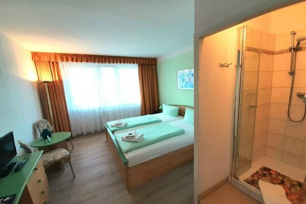 A hotel room with a bed, a desk with a chair, a laptop, a shower, and a window with curtains. - Hotel John Brinckman (Boltenhagen)
