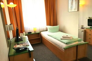 Una habitación pequeña con cama individual, escritorio, lámpara, espejo y televisión.