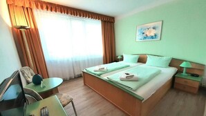 Habitación de hotel con una cama, un escritorio con silla, una lámpara y un cuadro en la pared.