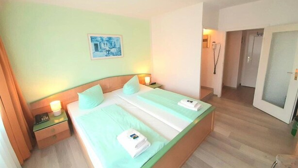 Una habitación de hotel con cama, mesitas de noche, un cuadro y la puerta del baño.