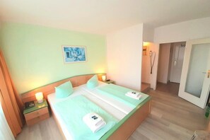Una habitación de hotel con cama, mesitas de noche, un cuadro y la puerta del baño.