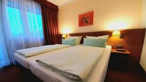 Habitación de hotel con una cama grande, dos mesitas de noche, un cuadro colgado en la pared y una ventana con cortinas.