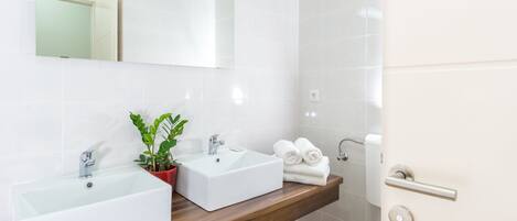 A bathroom with two sinks, a mirror, a potted plant, and towels on the counter.